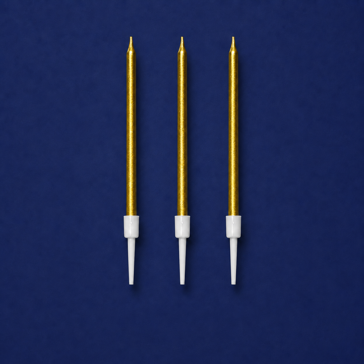 Set of three metallic gold cake candles with white holders on a blue background