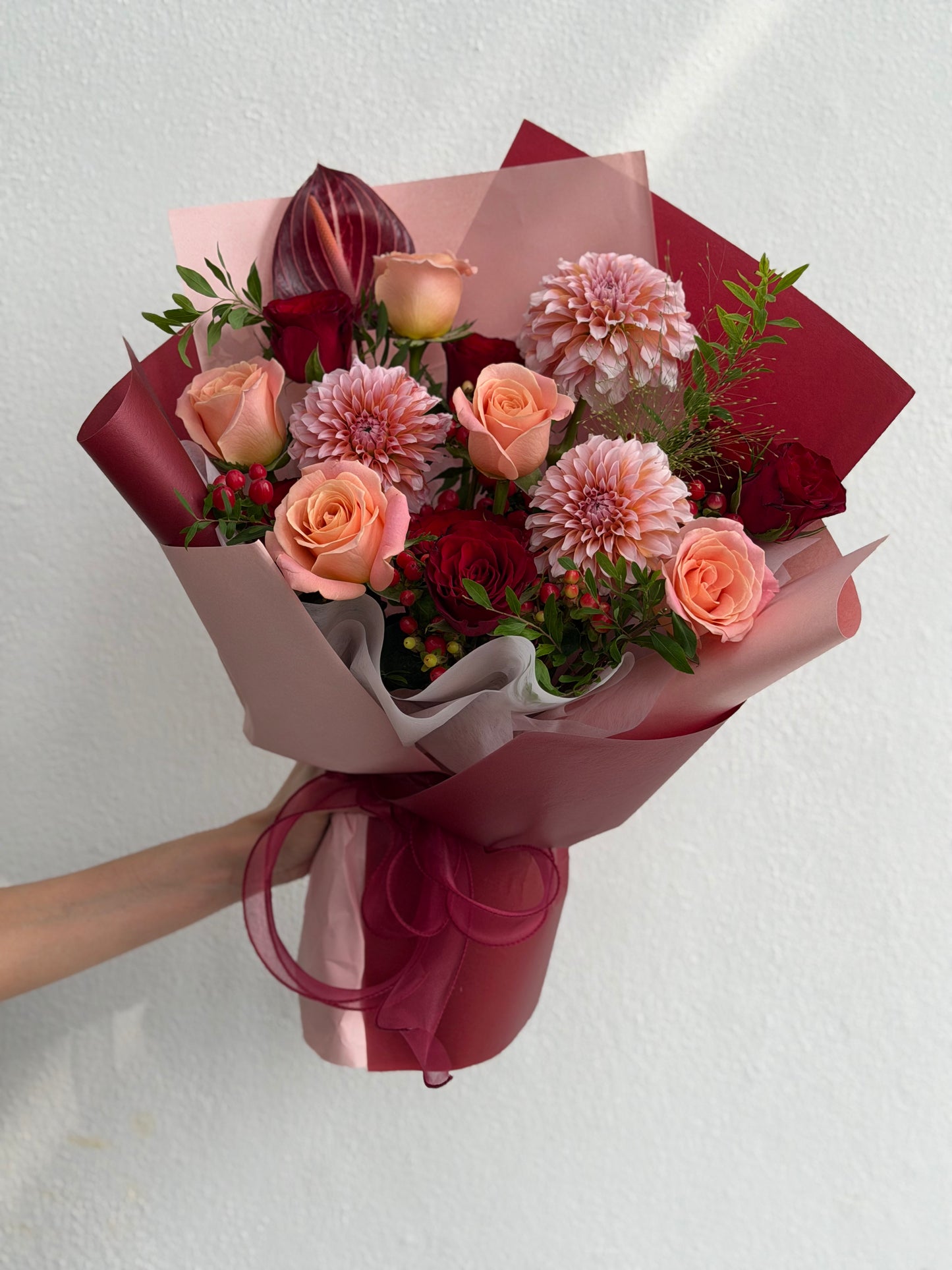 Beautifully arranged floral bouquet featuring pink and red roses, chrysanthemums, and green foliage, wrapped in elegant dusty pink and deep red paper with a matching ribbon. | Miyabi Cakery