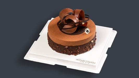 Miyabi Dark Muse chocolate cake with cocoa-dusted top and sculpted chocolate ribbons on a white board